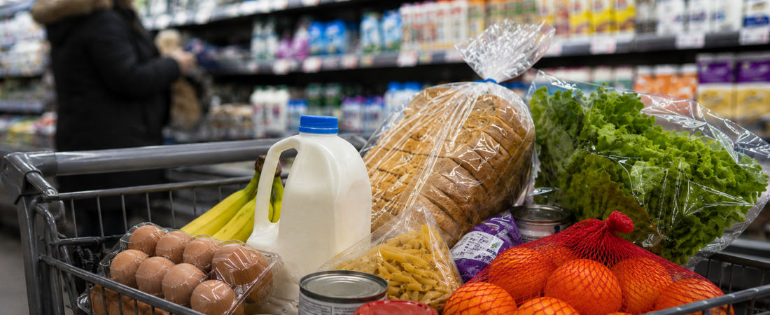 Carrinho de compras com bens alimentares essenciais num supermercado.