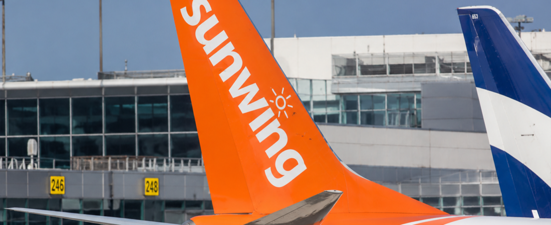 Cauda de um avião da Sunwing junto ao terminal de um aeroporto.